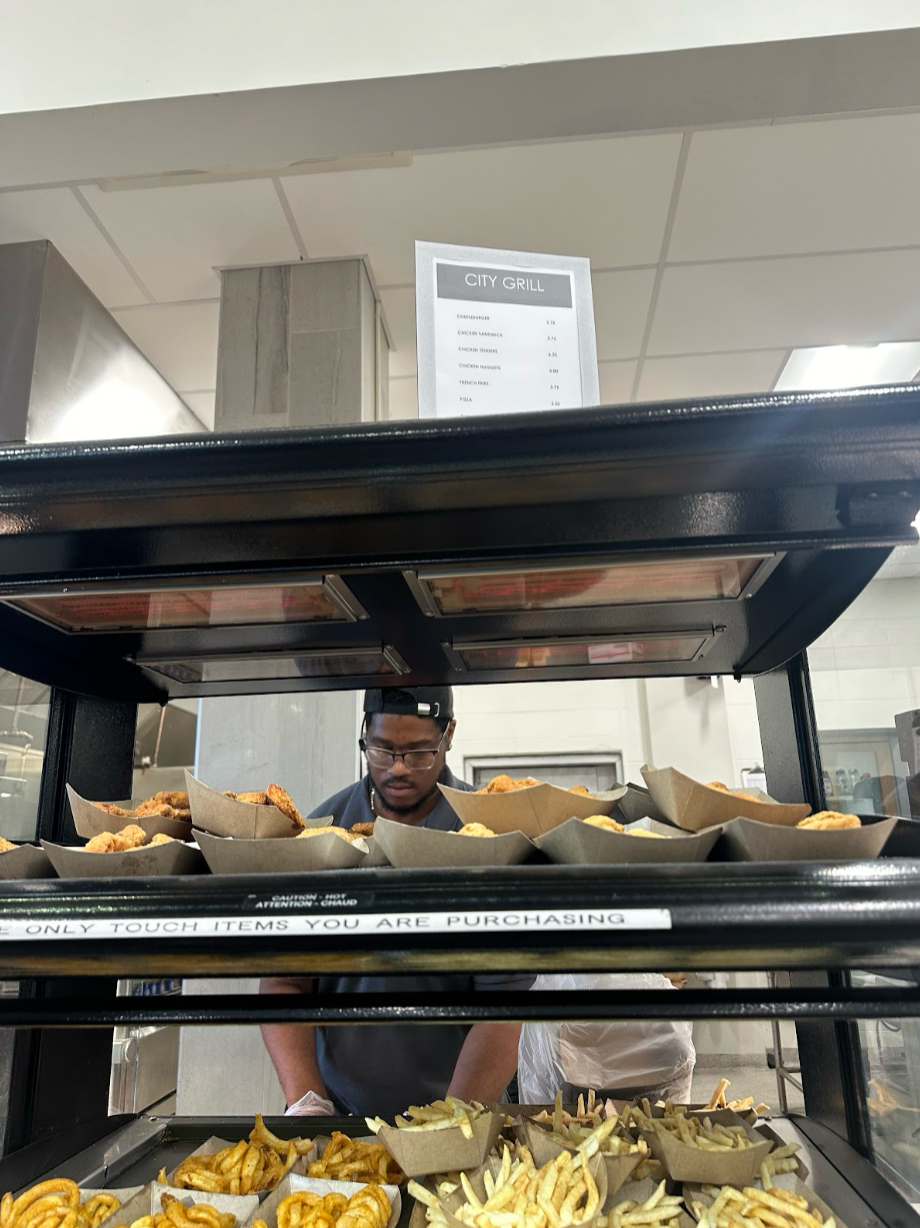 Handling the fried food section of the cafeteria, Rob Barlow places the chicken fingers and fries into the display right before the rush of second lunch. Students have regardless of the pricing backlash. 