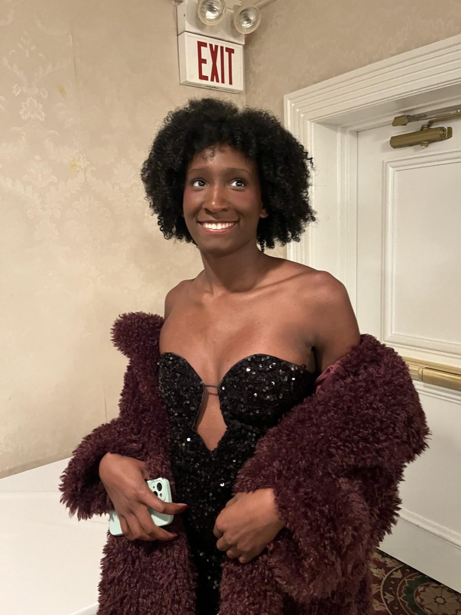 Lauren Montgomery looks off into the distance in a black shimmery dress with a red fur coat.