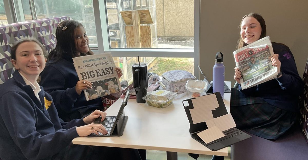 Erin Olimpo ‘25, Halo Hall ‘27, and Ava Brinkerhoff ‘25 hold up a newspaper while celebrating an Eagles’ win.