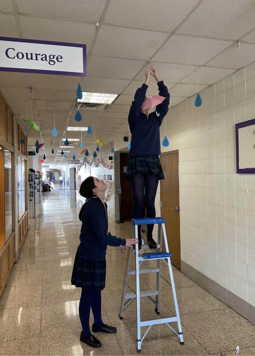 Art  association member, Elodie Breslin ‘27(visual arts) and Silvia Robinson ‘26 (cast member) helping put up the umbrellas and raindrops in the hall way for fall musical, “Singing in the Rain”